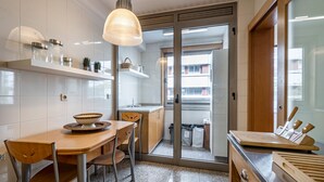Una cocina con una mesa de madera, sillas, una lámpara colgante y vistas al exterior a través de un ventanal.