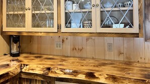 Ett kök med träskåp, en kaffebryggare och hyllor med glasskivor där köksredskap förvaras.