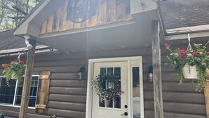 En timmerstuga med en skylt som visar ordet ”BUNKHOUSE”, en vit dörr och hängande blomkorgar.