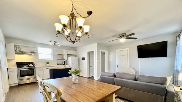 A modern kitchen with a dining area, a gray sofa, and a ceiling fan. - Point on Pollock - Brewery Row - Brim of Downtown (New Bern)