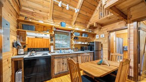 L’intérieur d’un chalet en bois comprend une cuisine, un coin repas et une fenêtre donnant sur une forêt.