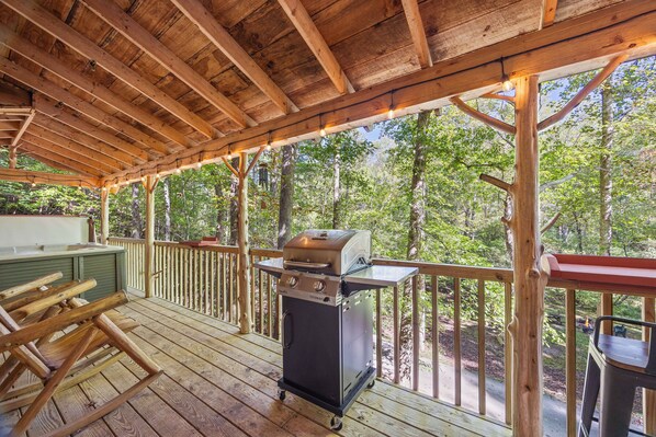 Une terrasse extérieure couverte, équipée d’un barbecue, de rampes en bois et offrant une vue sur une zone boisée.