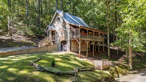Une cabane rustique dotée d’une terrasse en bois et d’un toit en métal, entourée d’une zone boisée.