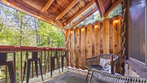 Une terrasse en bois avec des sièges d’extérieur, une table avec des chaises et une vue sur la forêt.