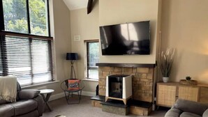 A living room with a fireplace, a flat-screen TV mounted above it, and a large window with blinds.