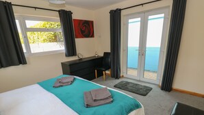 A hotel room with a bed, a desk, a chair, a view of the sea, and a painting on the wall. - Ty Mawr (Haverfordwest)