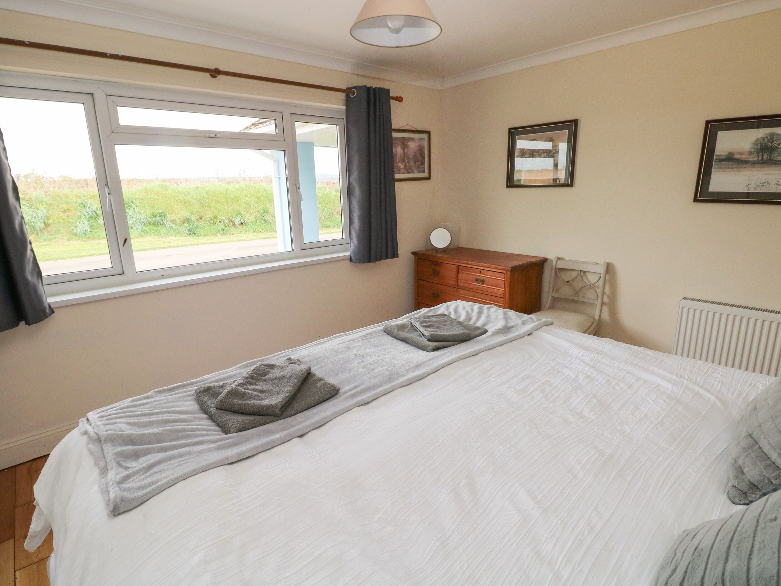 A bedroom with a large bed, a dresser, a chair, and a window with curtains.