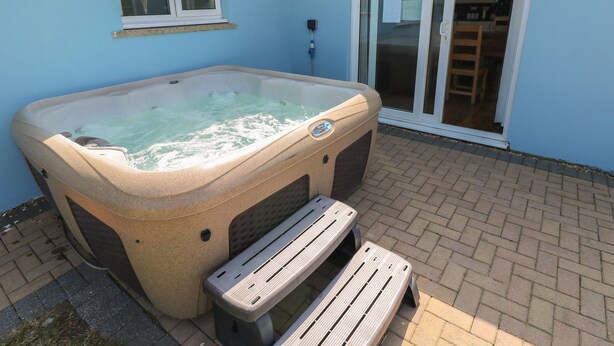 A hot tub in a covered outdoor area with a patio, a window, and a sliding glass door leading to a kitchen. - Ty Mawr (Haverfordwest)
