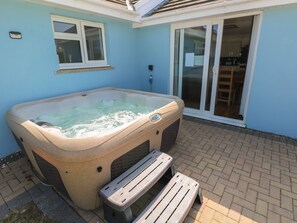 Un bain à remous situé dans un espace extérieur abrité, avec une terrasse, une fenêtre et une porte-fenêtre coulissante donnant sur une cuisine.
