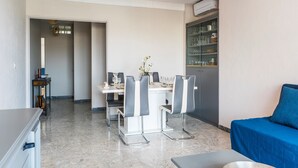 Un coin repas moderne avec une table et des chaises blanches, un vase rempli de fleurs et un meuble contenant de la verrerie.