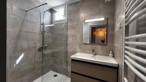 Une salle de bain moderne avec une douche à parois de verre, un meuble-lavabo avec un miroir et un porte-serviettes.
