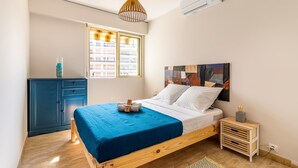 Une chambre à coucher avec un lit en bois, une fenêtre avec des stores, une armoire bleue et un climatiseur fixé au mur.