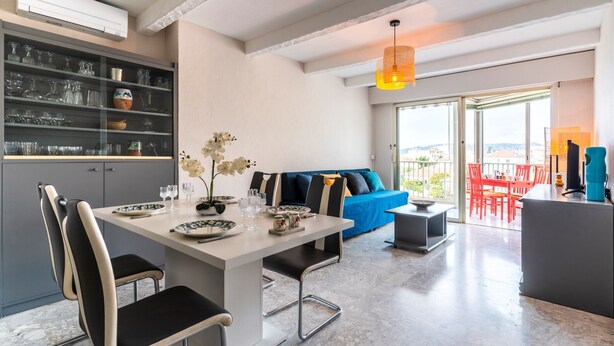 Un salon moderne comprenant un coin repas, un canapé avec des coussins, une table basse et une vue dégagée grâce à de grandes fenêtres.