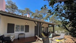 Un patio cubierto con mobiliario exterior, incluyendo sillas y una mesa, bajo un edificio blanco con techo de tejas.