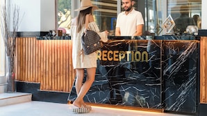 A reception desk with a wooden panel backdrop and a black marble surface. - Far Life Hotel (Konyaalti)