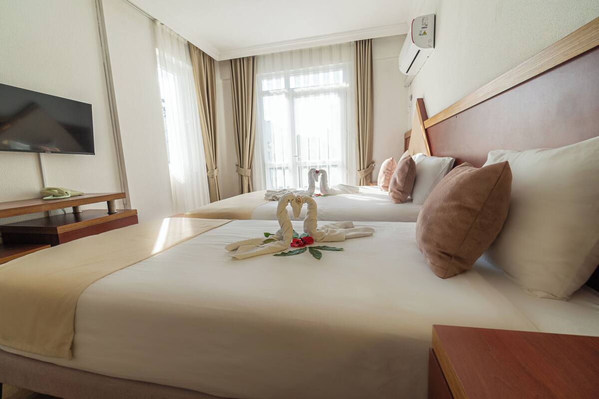 A hotel room with two beds, a flat-screen TV, a bedside table, and a window with curtains.