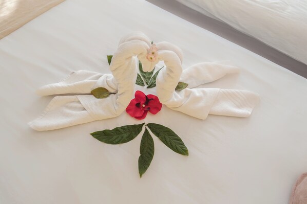 A neatly arranged towel sculpture with a red flower and green leaves on a bed. - Far Life Hotel (Konyaalti)