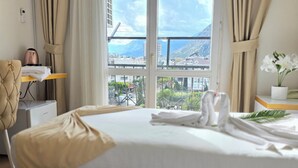 A hotel room with a bed, a chair, a table, an air conditioner, a potted plant, and a view of a mountainous landscape. - Far Life Hotel (Konyaalti)