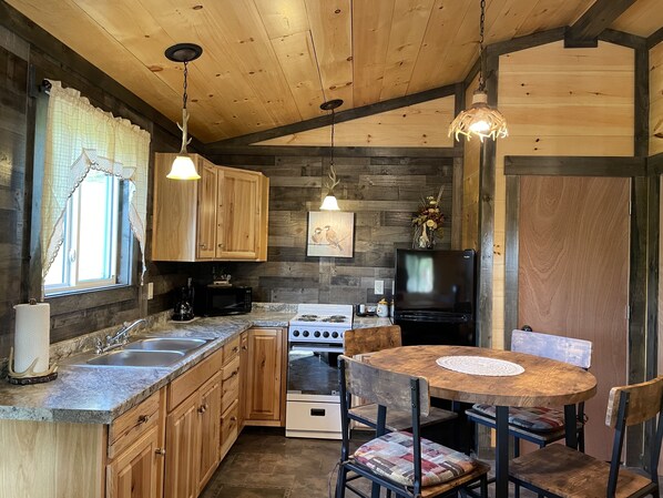 A rustic kitchen with wooden cabinets, a stove, a microwave, a sink, and a dining table with chairs.