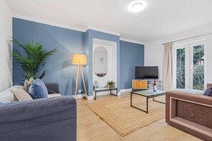 A modern living room with a sofa, a coffee table, a floor lamp, and a television. - 3 Bed House Sleeps 8 -near Heathrow -free Parking (Hounslow)