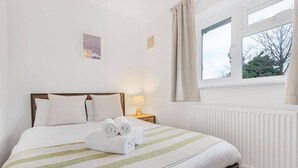 A hotel room with a bed, a window with curtains, a radiator, and a wall-mounted lamp. - 3 Bed House Sleeps 8 -near Heathrow -free Parking (Hounslow)