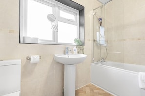 Un baño con lavamanos blanco, espejo, inodoro y zona de ducha.