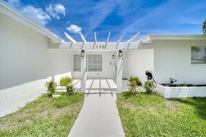 Una casa moderna con facciata bianca, un numero 1401 e un portico coperto, con un piccolo giardino.