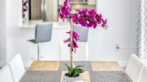 En matplats med ett träbord, grå bordsunderlägg, vita stolar och en bordsdekoration bestående av lila orkidéer.