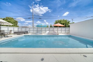Una piscina con lettini e ombrelloni, circondata da un recinto bianco e un cielo sereno.