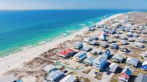 Vista aérea de una zona residencial costera con casas a lo largo de la playa, aguas azul turquesa y una playa de arena.