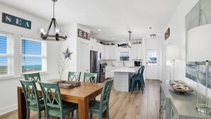 Una cocina moderna con armarios blancos, una isla central y una zona de comedor con sillas verdes.