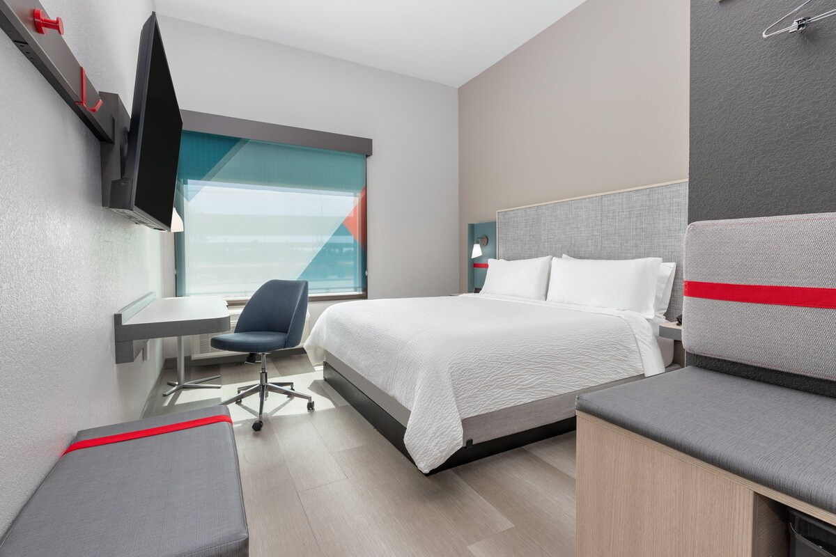 A modern hotel room with a bed, desk, chair, and a TV mounted on the wall.