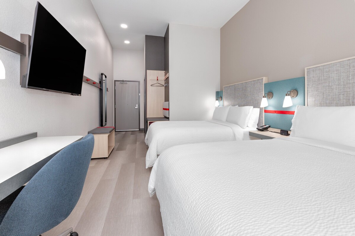A hotel room with two beds, a desk, a TV mounted on the wall, and a wardrobe.