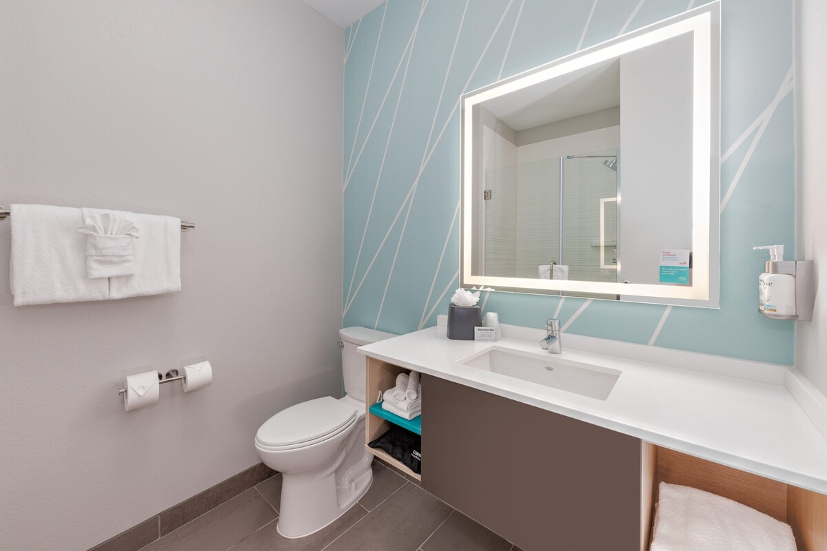 A modern bathroom with a white toilet, a sink with a mirror above it, and a towel rack with towels.