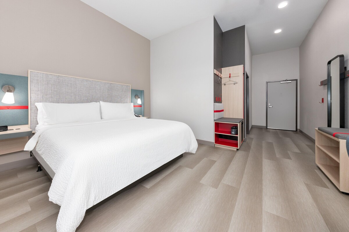 A modern hotel room with a large bed, bedside tables, a wardrobe, and a mirror.