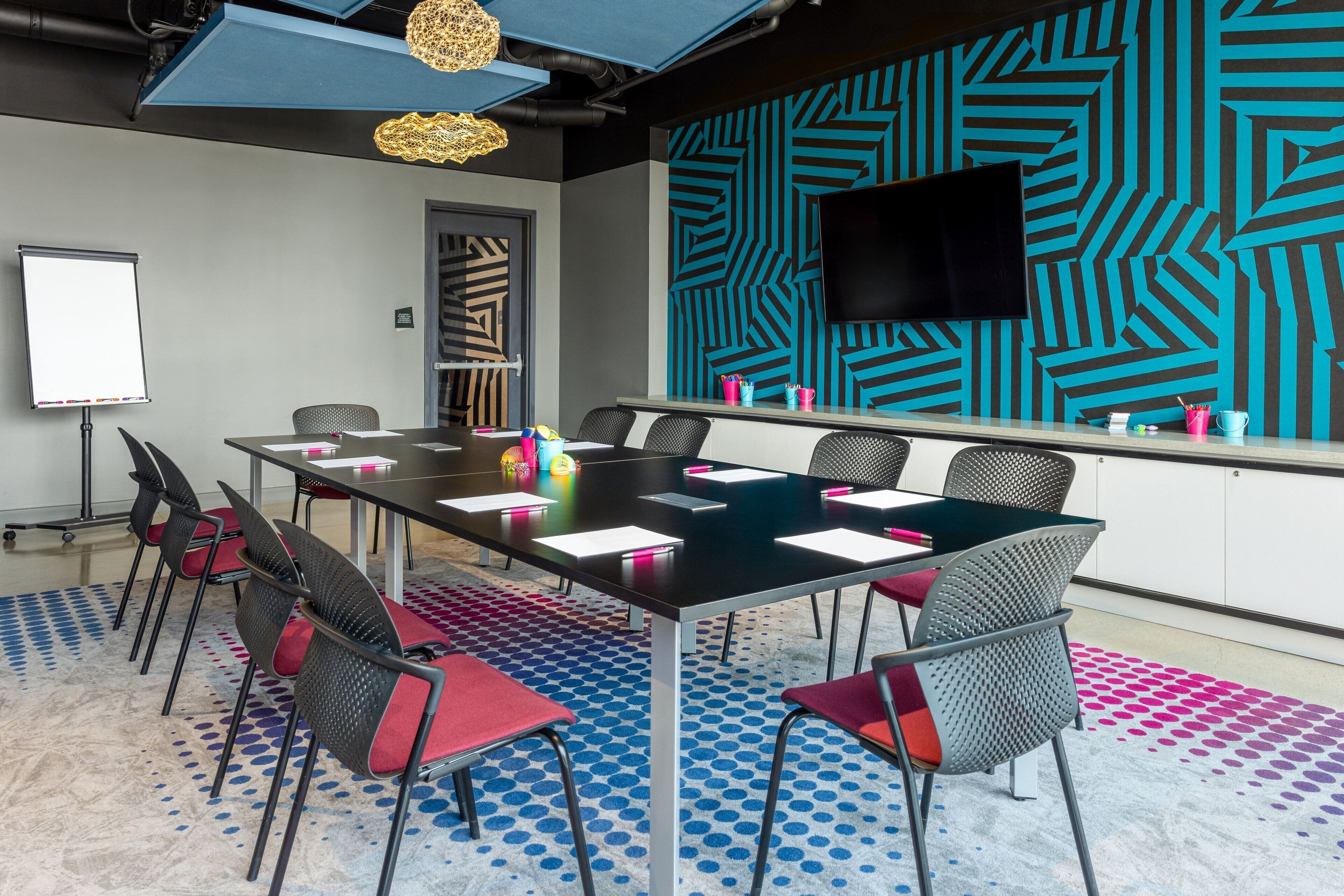 A conference room with a large table, chairs, a whiteboard, and a TV on the wall.
