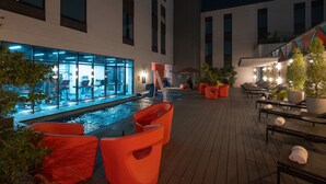 An indoor pool area with orange chairs and tables, a glass wall, and a staircase leading to upper floors. - Aloft by Marriott San Pedro Sula (San Pedro Sula)