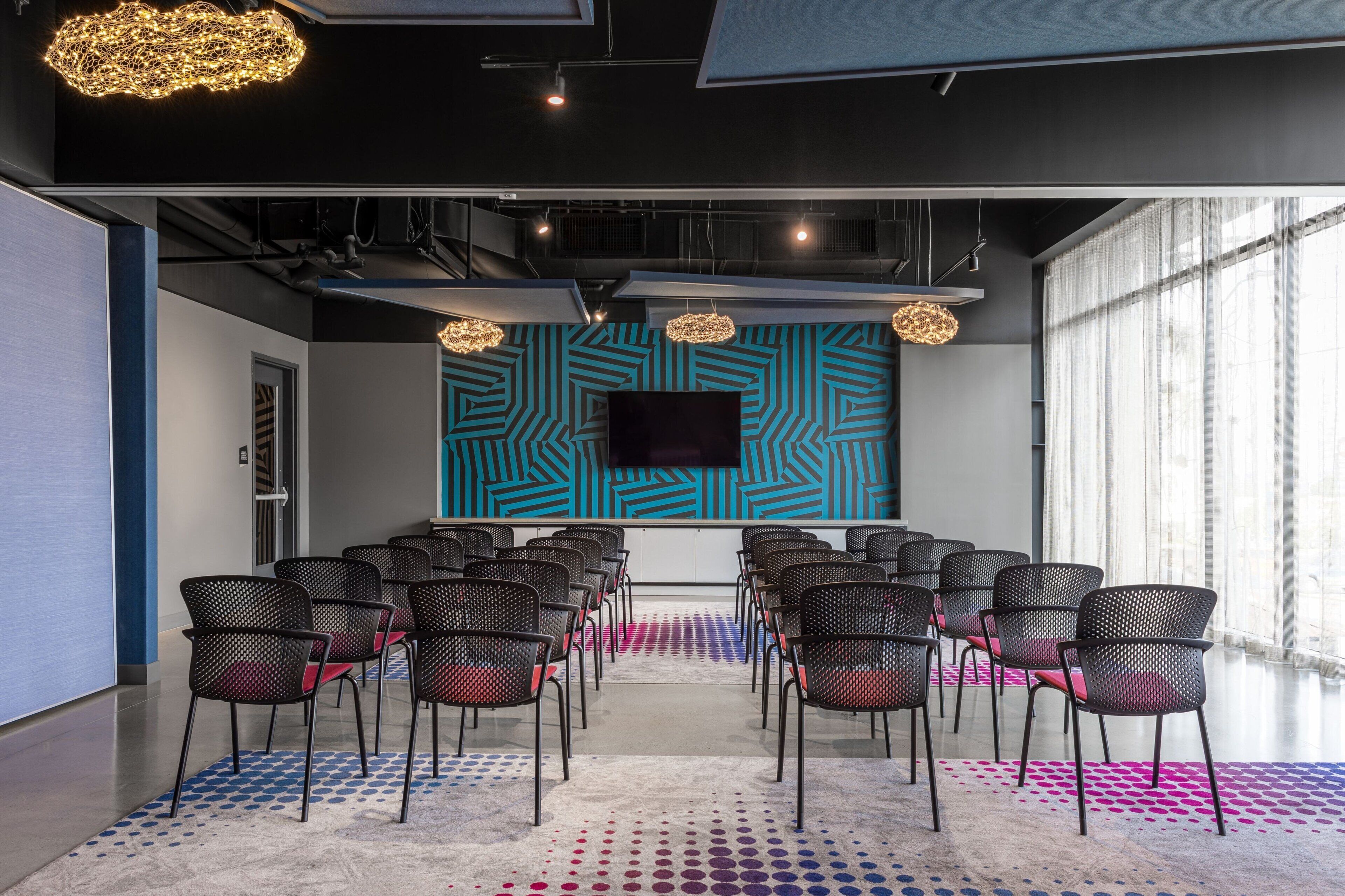 Een congreszaal met rijen stoelen, een groot scherm en een behang en vloerkleed met een patroon.