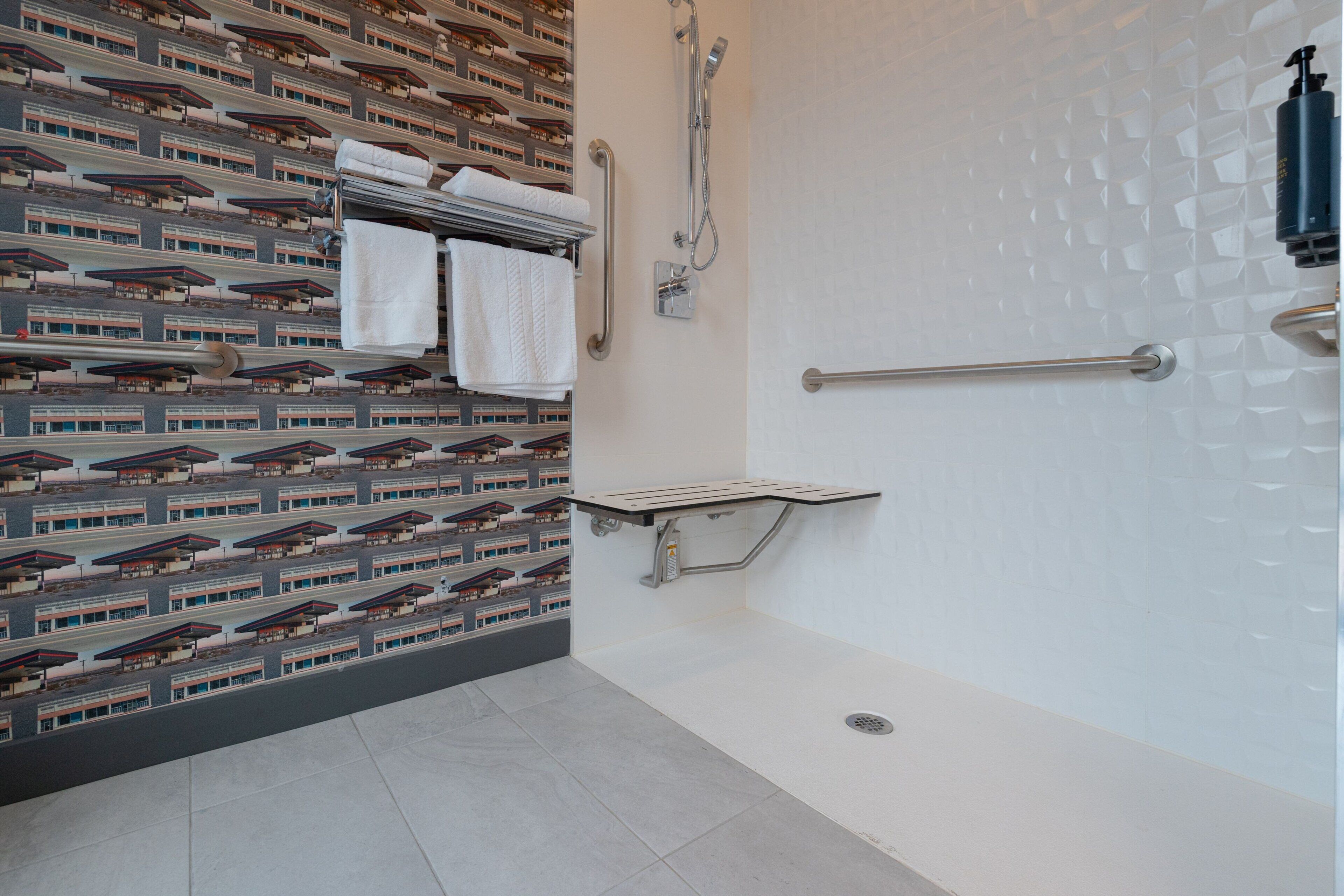 A modern bathroom with a patterned wall, a shower area, and a towel rack with folded towels.