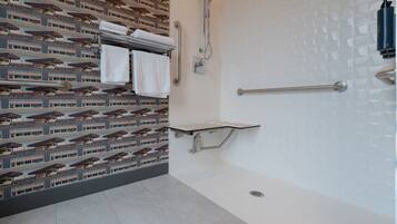 A modern bathroom with a patterned wall, a shower area, and a towel rack with folded towels.