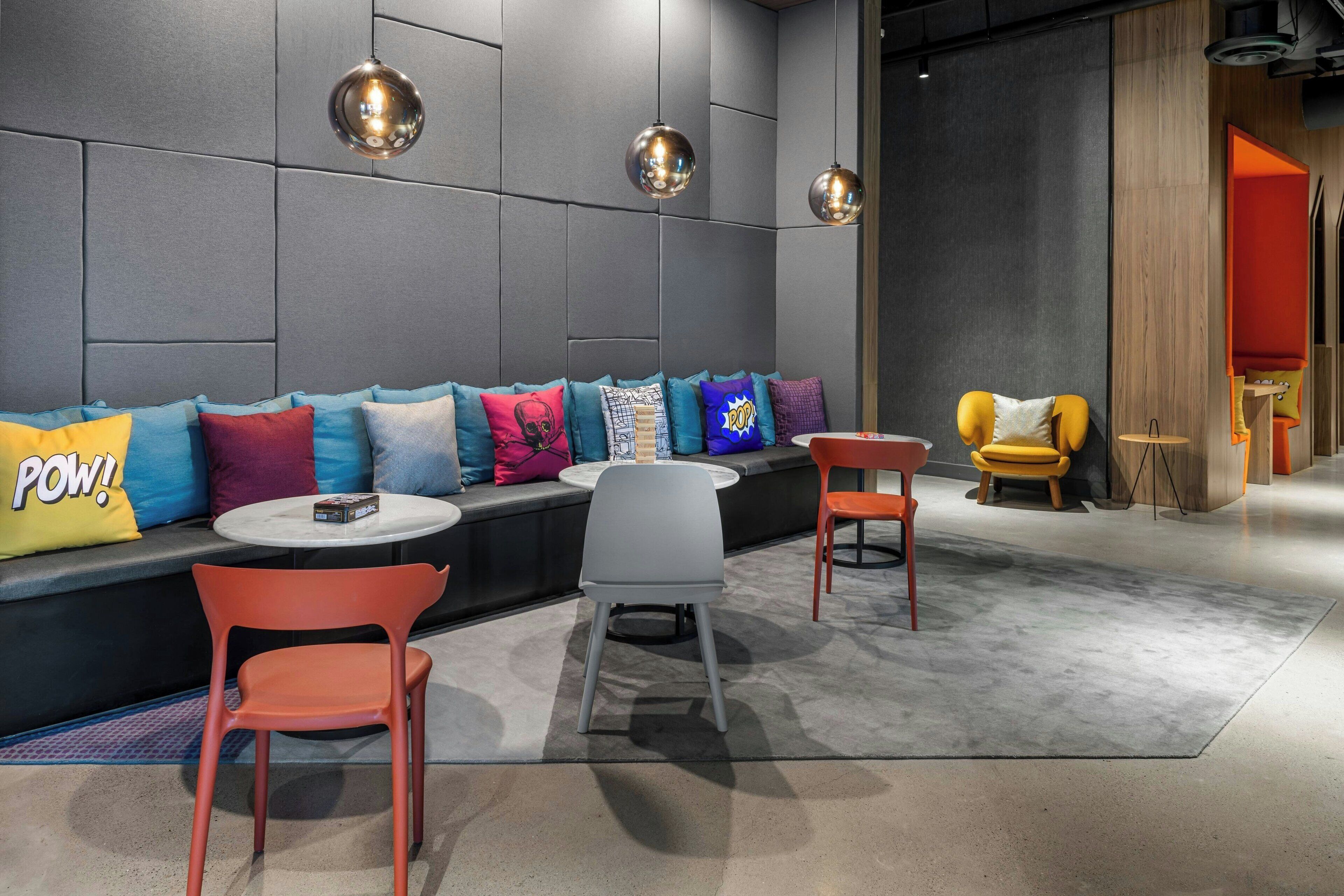 A modern lounge area with a sofa adorned with colorful pillows, a round coffee table, and two chairs.