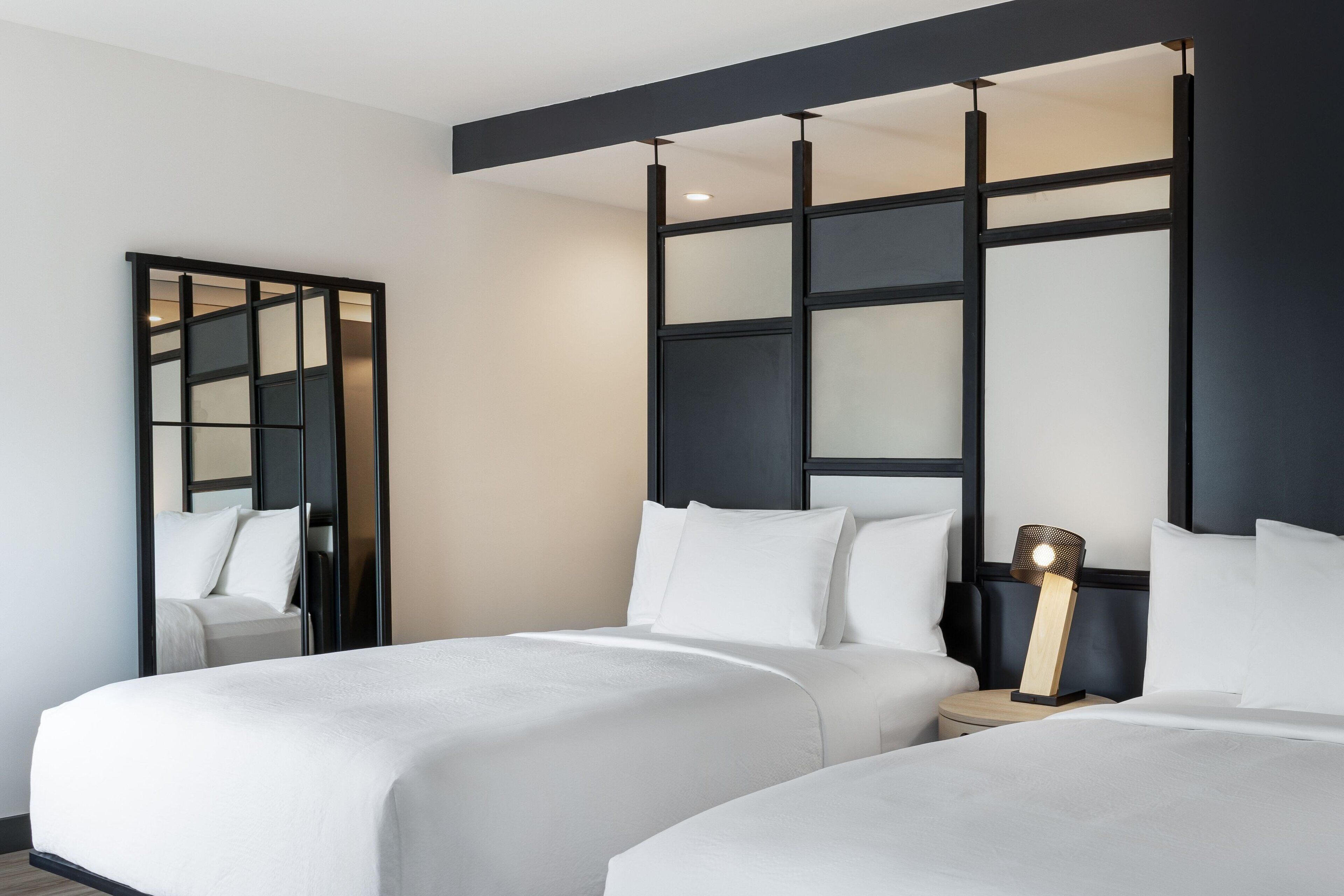 A hotel room with two beds, a large mirror, and a nightstand with a lamp.