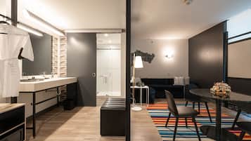 Una habitación de hotel moderna con kitchenette, una zona de comedor con una mesa redonda y sillas, un sofá y un colorido tapete a rayas.