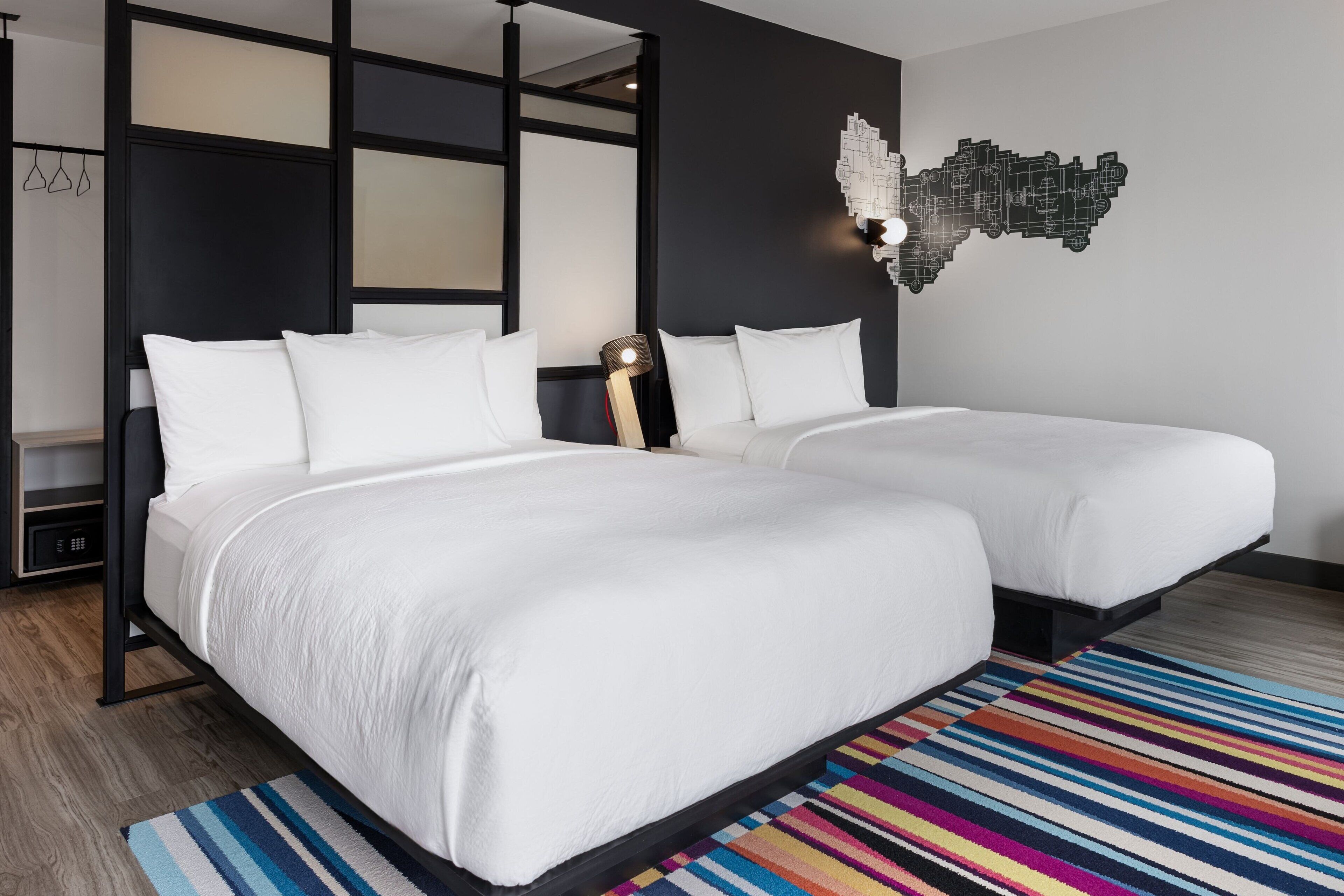 Una habitación de hotel moderna con dos camas, un colorido tapiz a rayas y una original obra de arte en la pared.