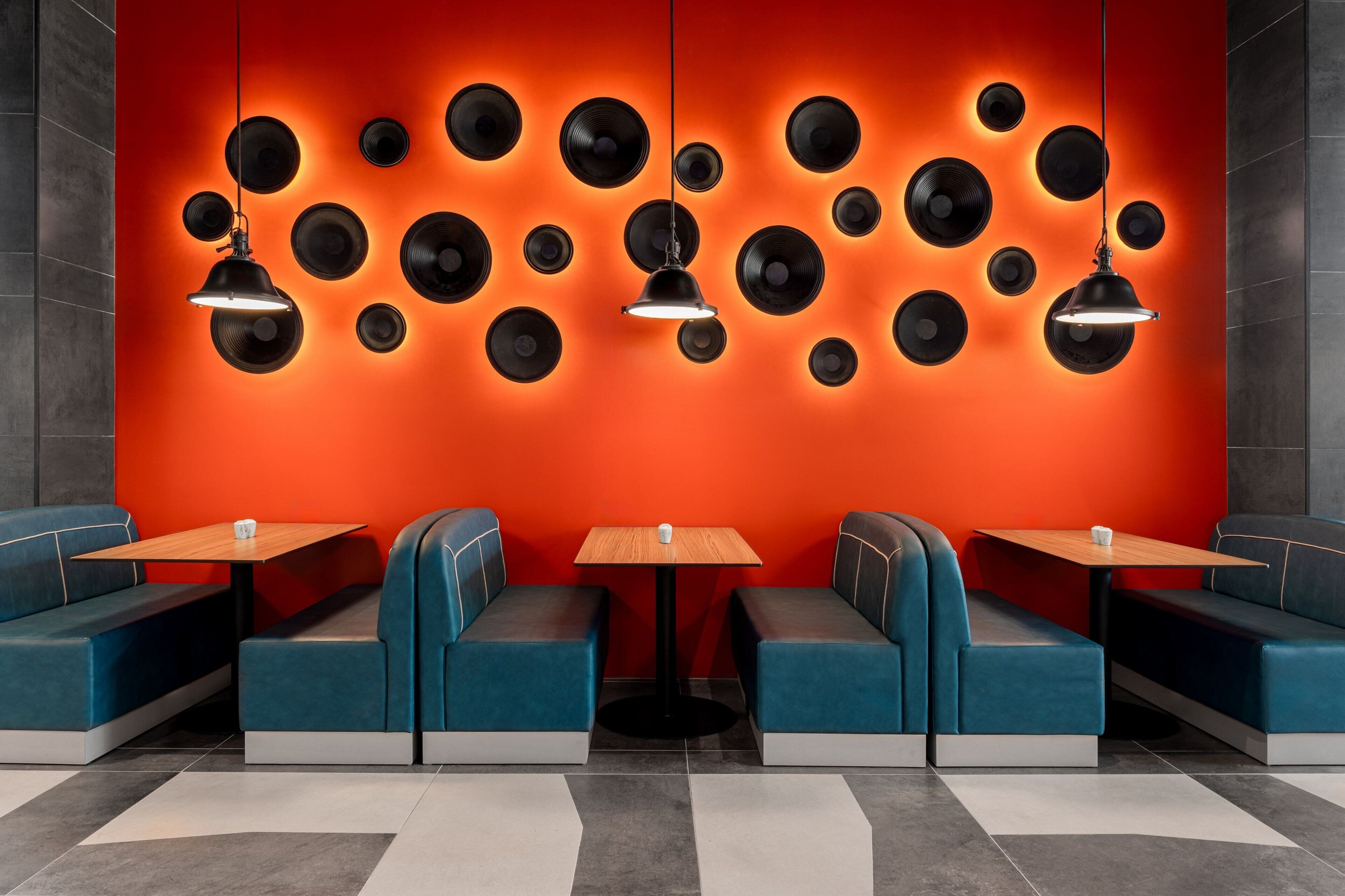 A modern restaurant with blue booths, a central table, and a wall of illuminated vinyl records.