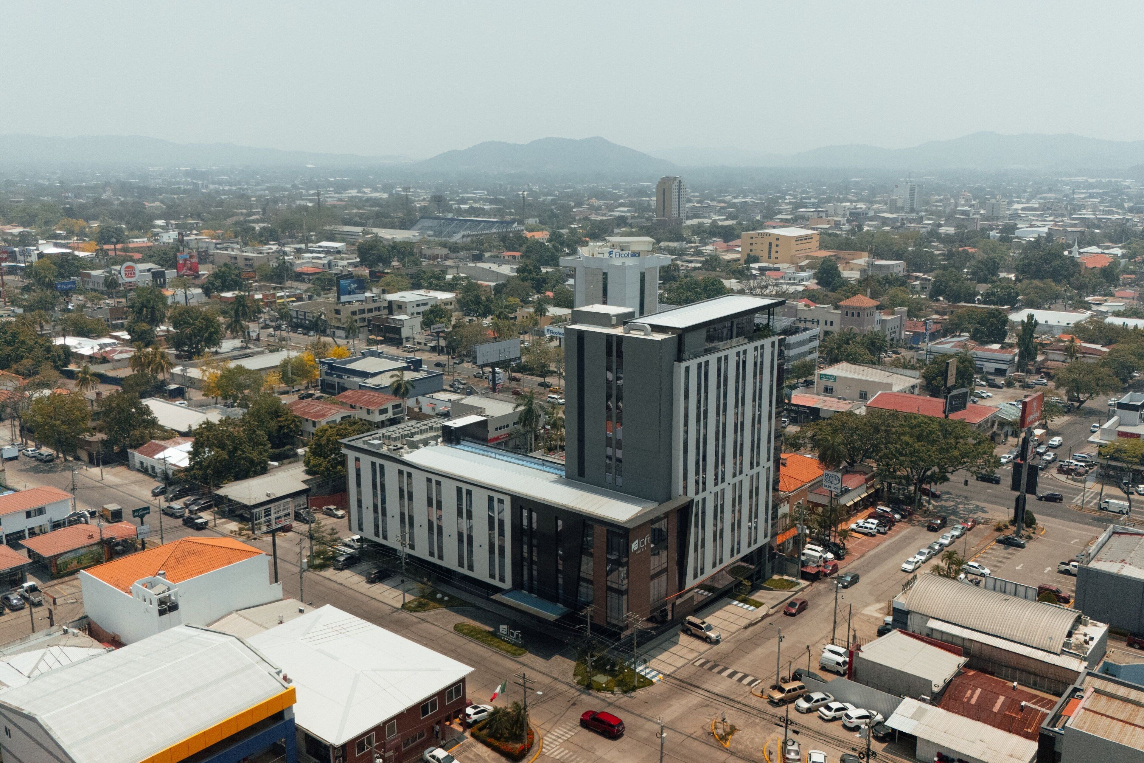 A modern building with a prominent tower, surrounded by a dense urban area with various buildings and streets.