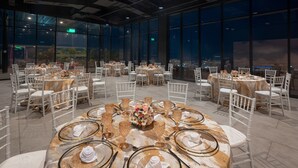 A spacious indoor dining area with multiple round tables set for events, large windows offering a city view, and a modern industrial ceiling design. - Aloft by Marriott San Pedro Sula (San Pedro Sula)