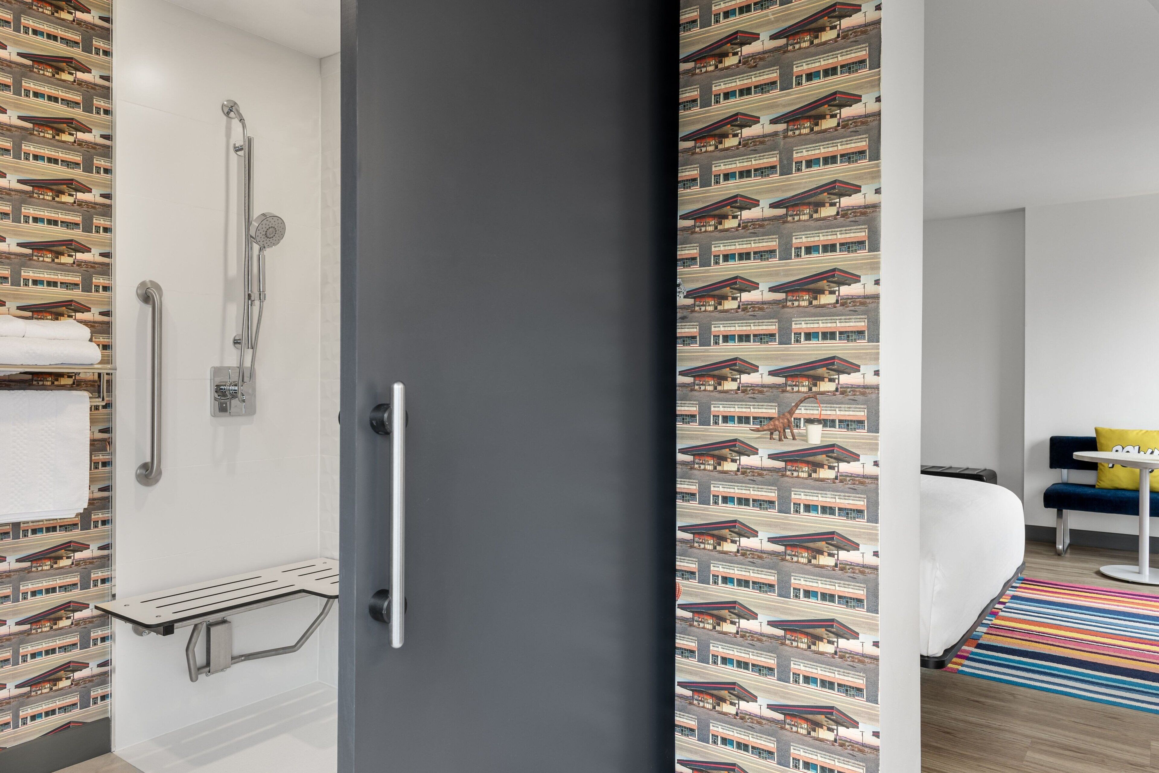 Een moderne hotelkamer met een douche, een bankje en een bed met een kleurrijk gestreept vloerkleed.