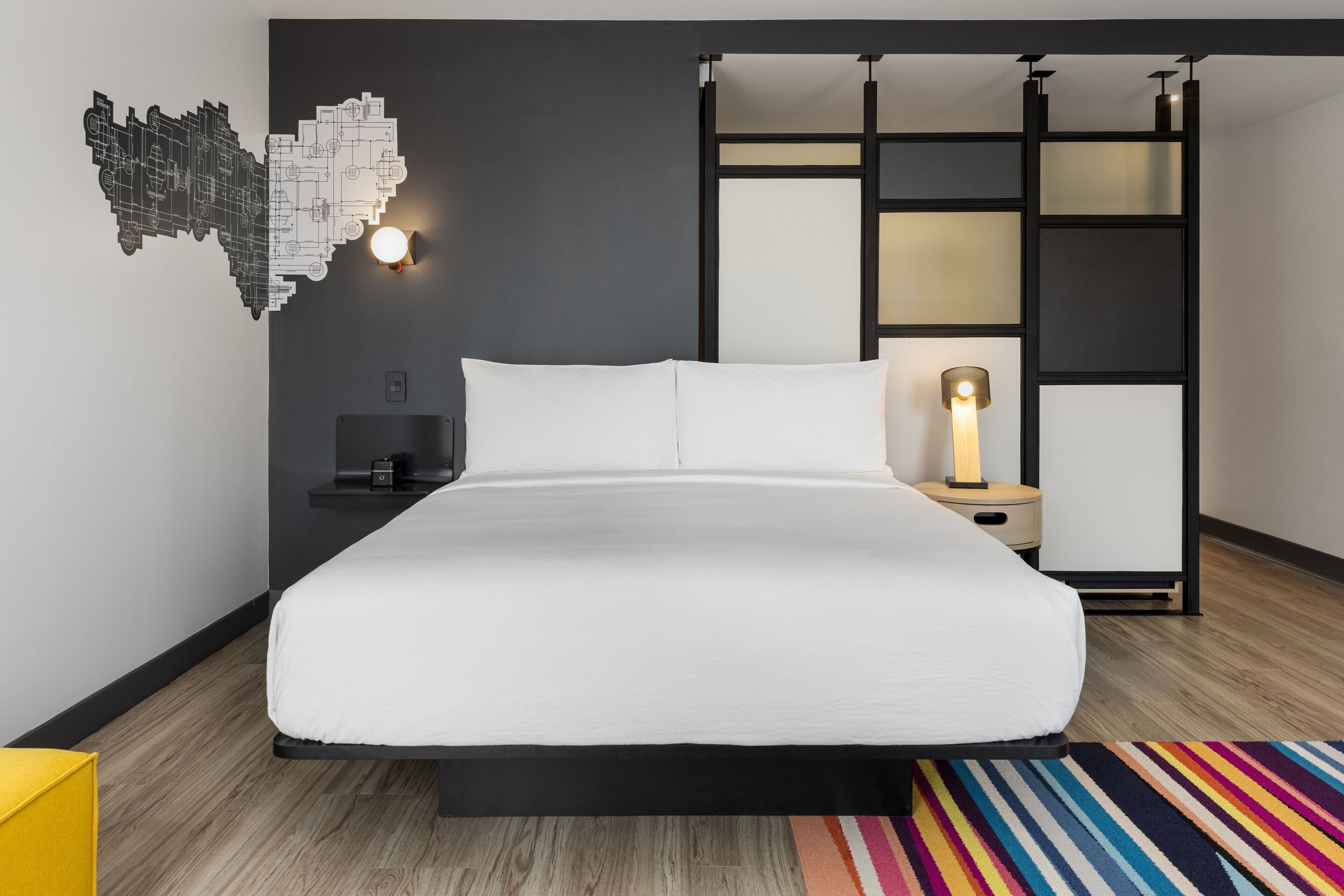 Quarto moderno com uma cama grande, uma mesa de cabeceira, uma luminária na parede e um objeto decorativo na parede.