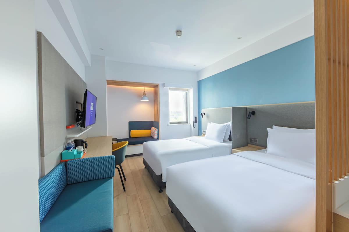 Une chambre d’hôtel avec deux lits, un bureau avec une chaise, une télévision et une fenêtre donnant sur un paysage agréable.